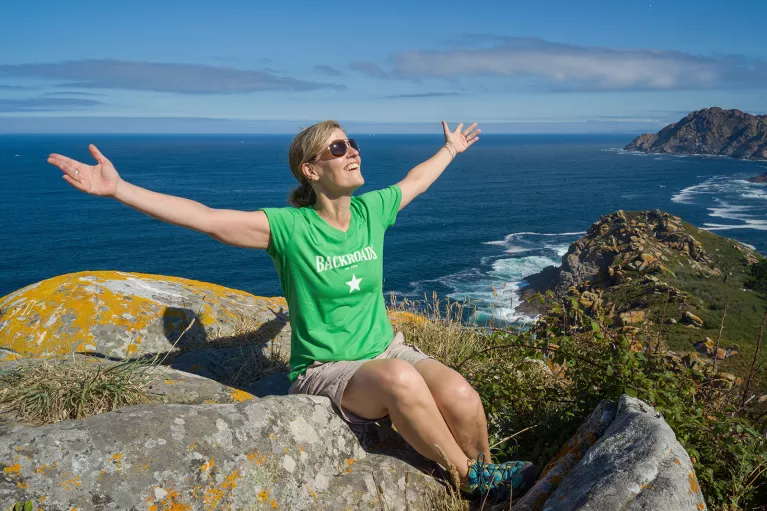 Guest on sunny hilltop, arms outstretched, ocean behind them.