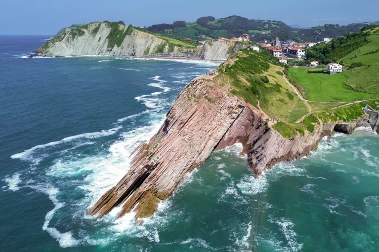Slanted cliff on the coast of an ocean, with a small town in the distance