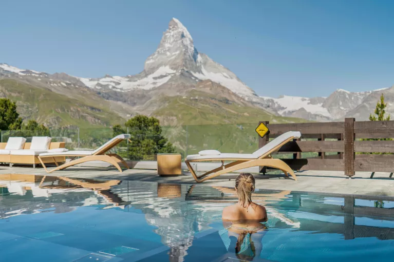 Woman swimming in an outdoor pool looking out towards a tall mountain