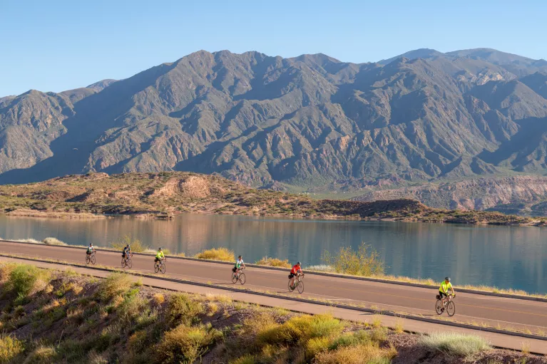 people biking down a road by a mountain range