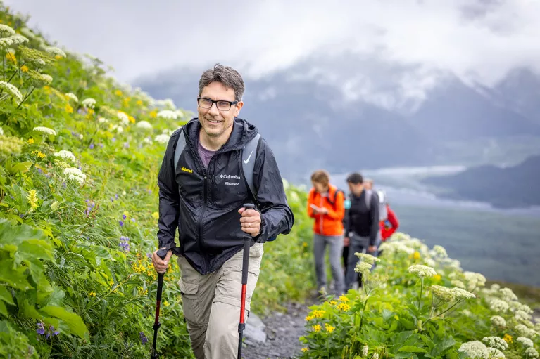 Man with walking sticks climbing up grassy hill