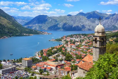 Aerial view of buildings all along the shore of a body of water, mountains in the distance