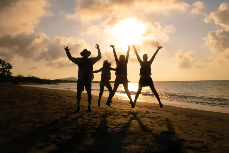 Three peoples silhouettes as they jump against the sunset