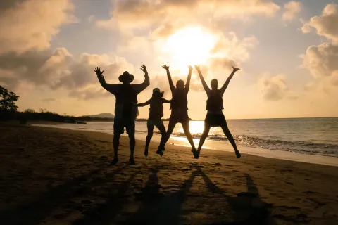 Three peoples silhouettes as they jump against the sunset