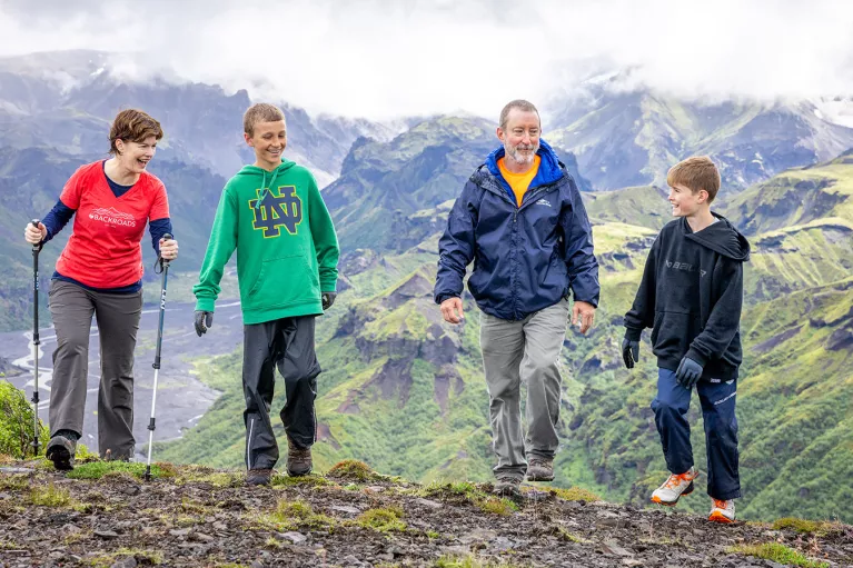 Man and women with two kids, walking on a dirt path with fog-covered mountains in the background