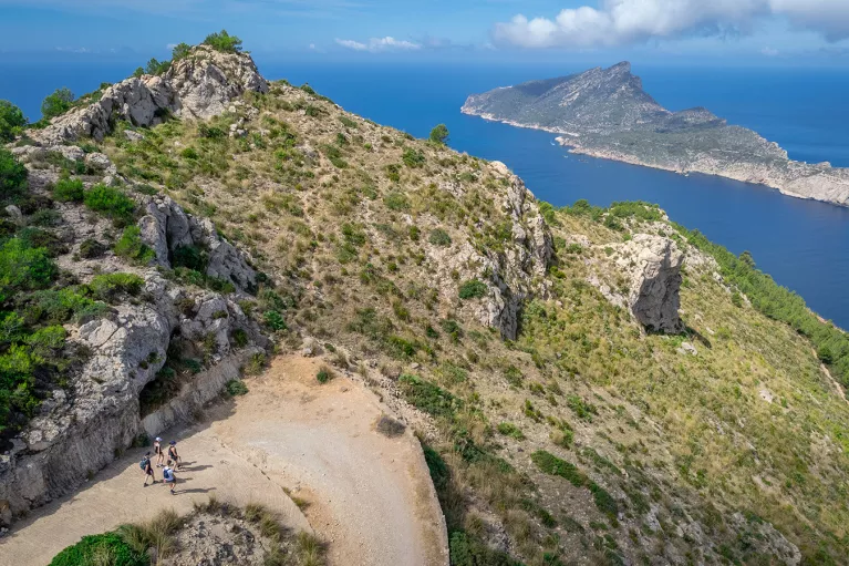 Group of people hiking on a trail along a cliff, with the ocean and an island in the distance
