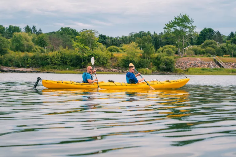 Two men inside of a yellow kayak, paddling in an open lake