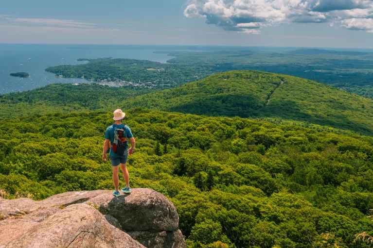 Man standing on the edge of a cliff, looking out towards a jungle