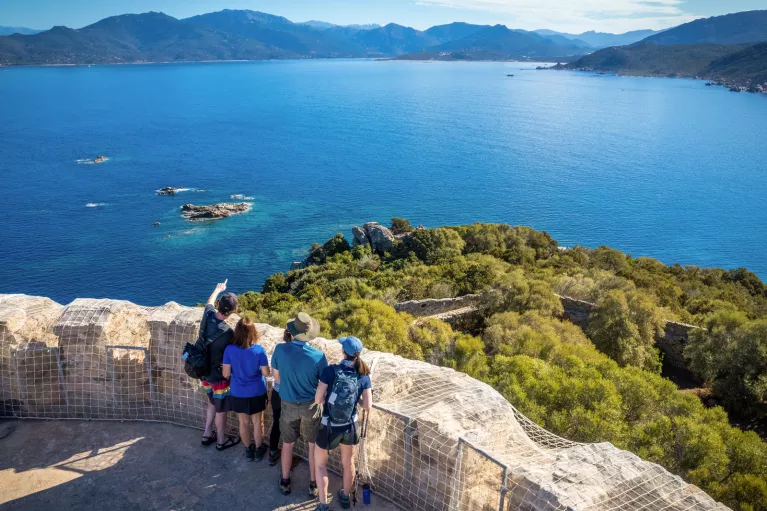 Group of men and woman on a tall rock path, overlooking to a large lake