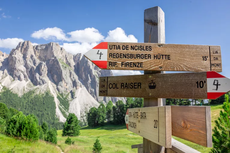 Wooden sign with red and white arrows, with tall rocky mountains in the background