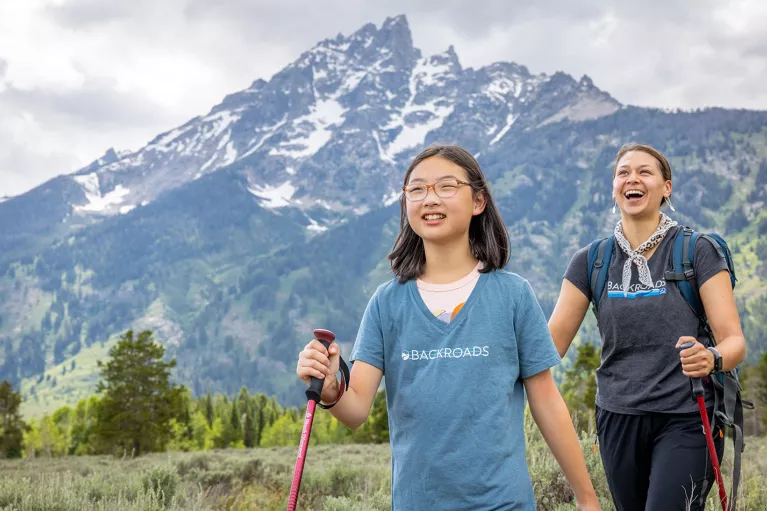 Woman and girl with walking poles hiking in a grassy valley