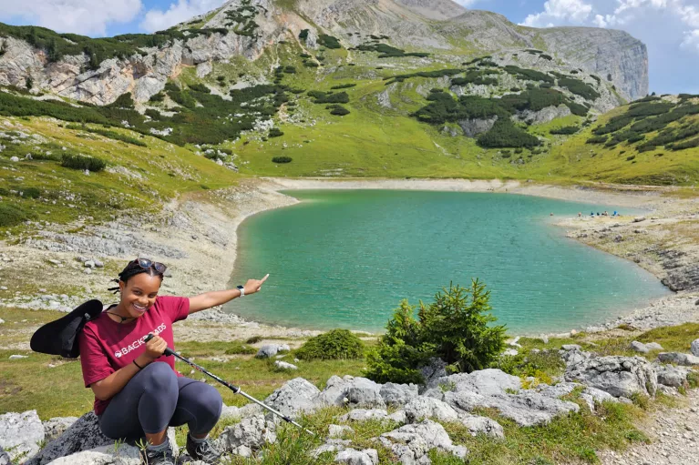 Woman sitting down and smiling, pointing at a small lake