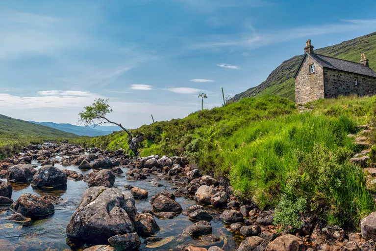 Boulders scattered through a river with a house on top of a small hill