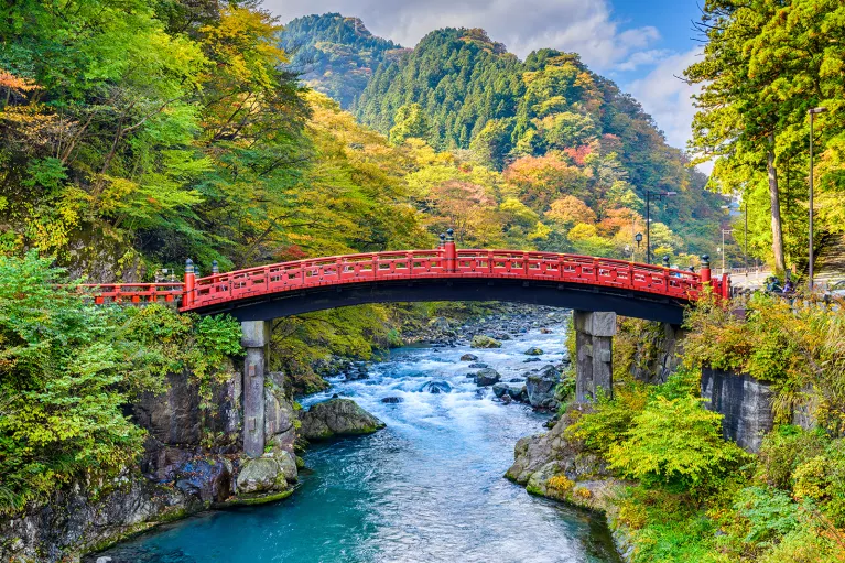 Red bridge over an active river, with large mountains in the background