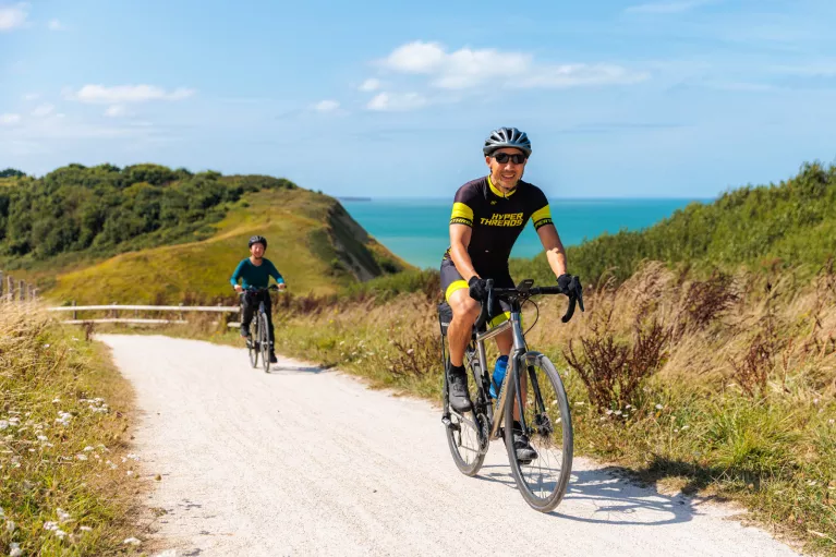 Man and woman biking on a sandy trail with the ocean in the background