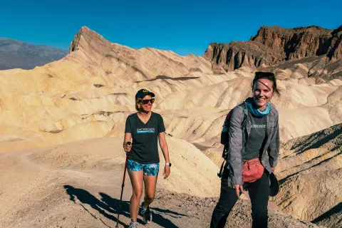 Two women ascending a rocky trail with large canyons in the background