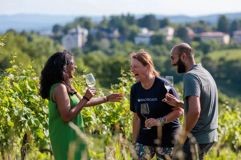 Two women and one man standing in a vineyard while holding glasses of wine