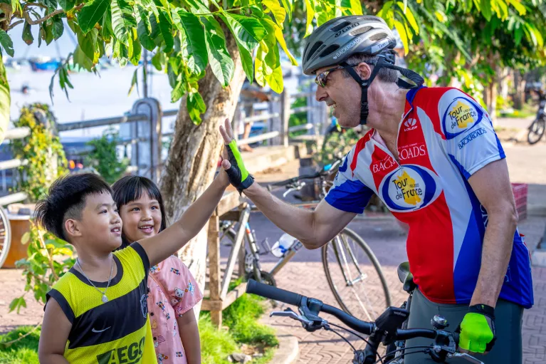 Man riding a bike while giving high fives to little kids