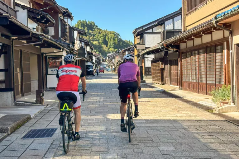 Two men biking on a stone road in the middle of a Japanese town
