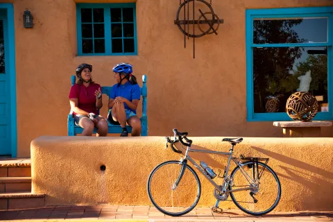 Two women sitting in front of an orange house, with a bike parked out front