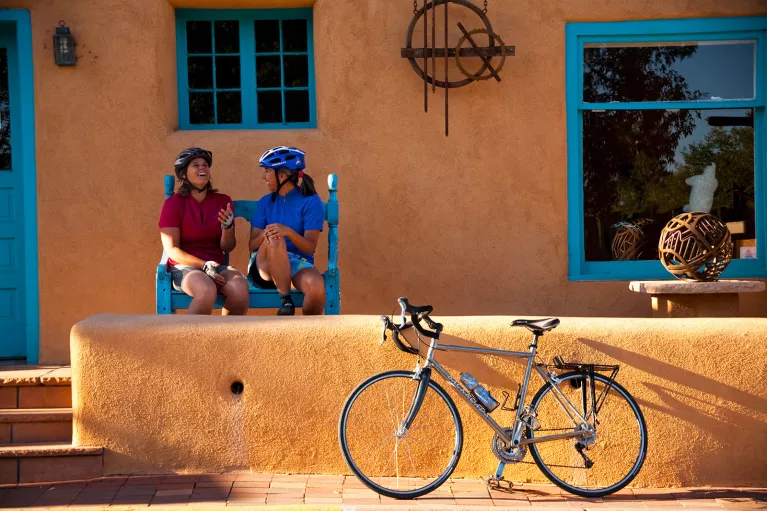 Two women sitting in front of an orange house, with a bike parked out front