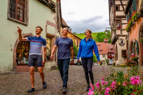 Two men and one woman walking on a stone alleyway, pointing and smiling