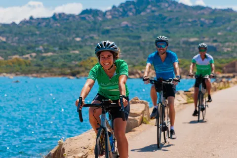 One woman and two men riding bikes on an empty road next to a large lake