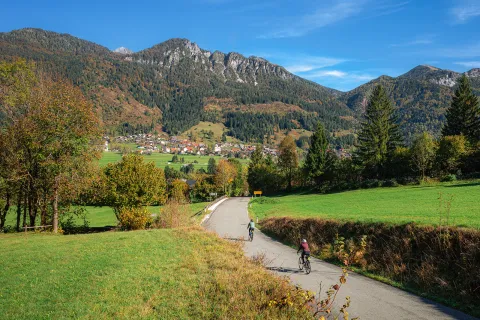 Two bikers on a road going towards a town and large mountains