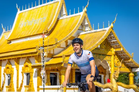 Man smiling while biking in front of a white and gold temple