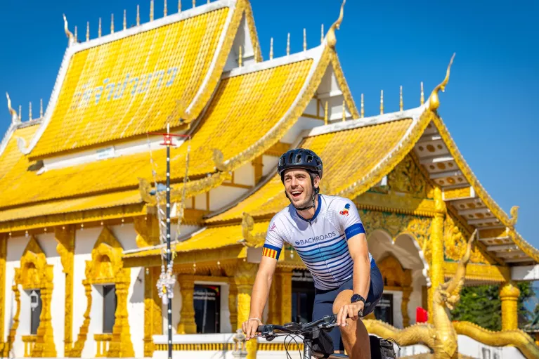 Man smiling while biking in front of a white and gold temple
