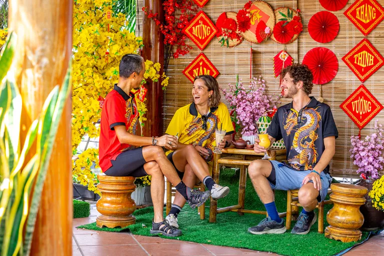 Two men and one woman sitting on wooden chairs in front of Vietnamese art pieces