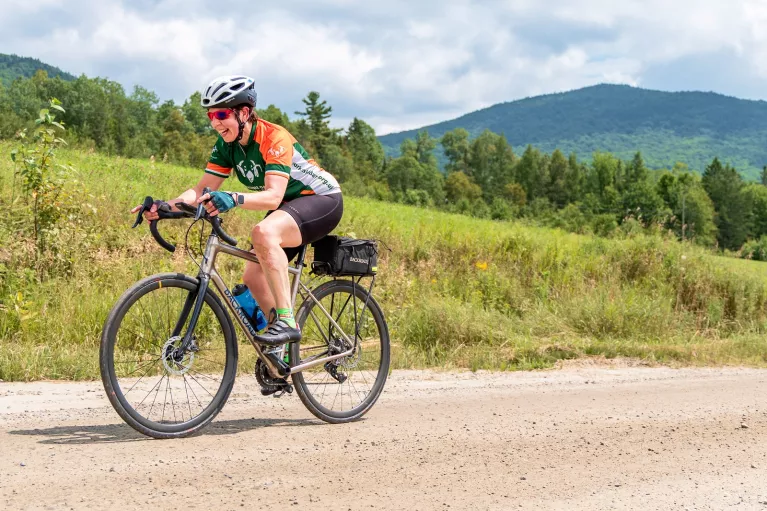 Woman riding a bike on a dirt road, with a grassy hill in the background