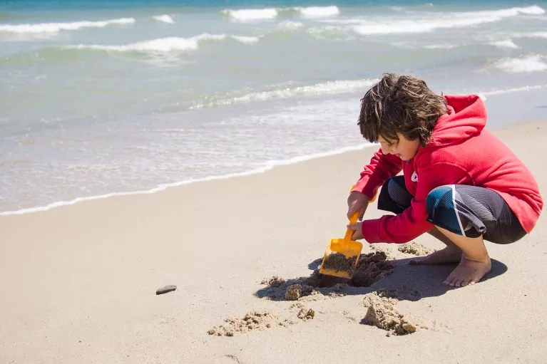 Boy on the beach, playing with the sand and a scooper