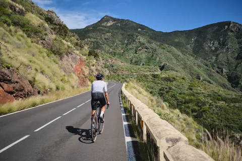 Person riding their bike on a road with large, grassy mountains in the distance