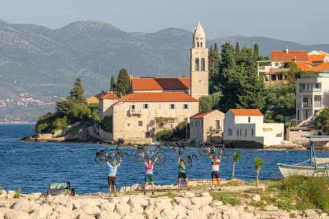 Group of people holding bikes over their heads, with a town and ocean in the background