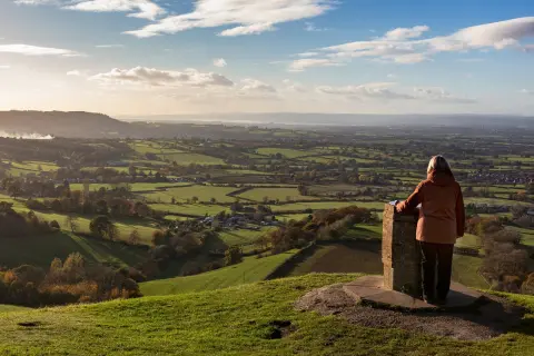Woman on top of a hill with a stone pillar looking out to a large valley