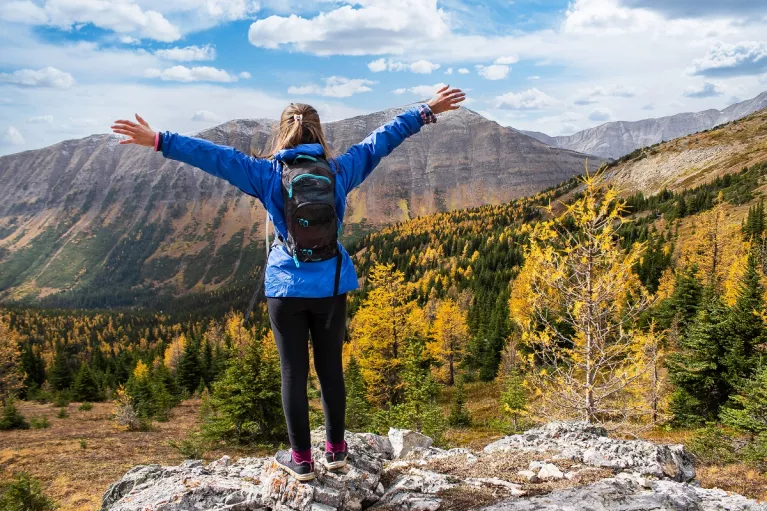 Woman wearing a blue jacket on top of a cliff with her arms wide open
