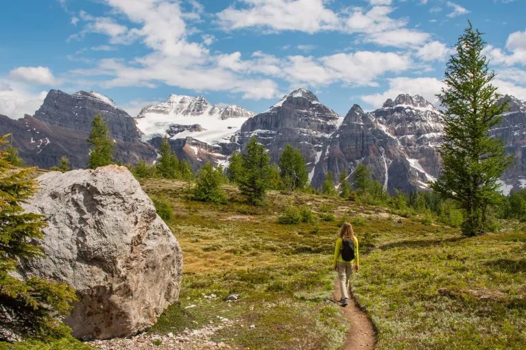 Woman walking along a dirt trail with large mountains in the distance