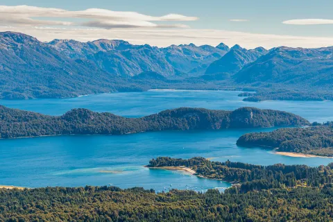Sky view of a large lake, surrounded by tall mountains and trees