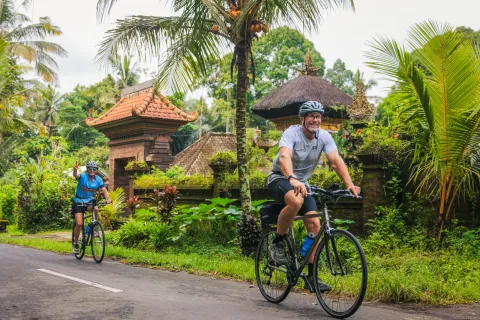 Man and woman biking on a road with jungle in the background