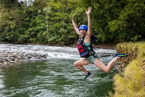 Woman wearing a helmet and life vest jumping into a lake