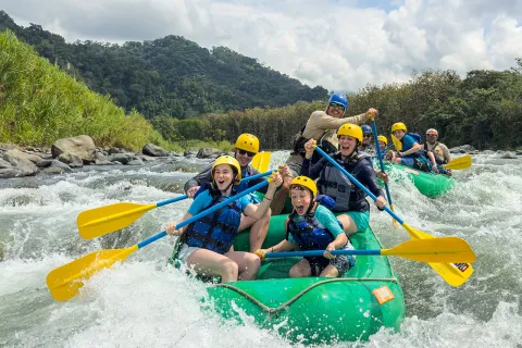 Two groups of families on green rafts, paddling in a river