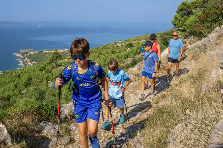 Group of kids with their parents hiking on a dirt and rock trail, with the ocean in the distance