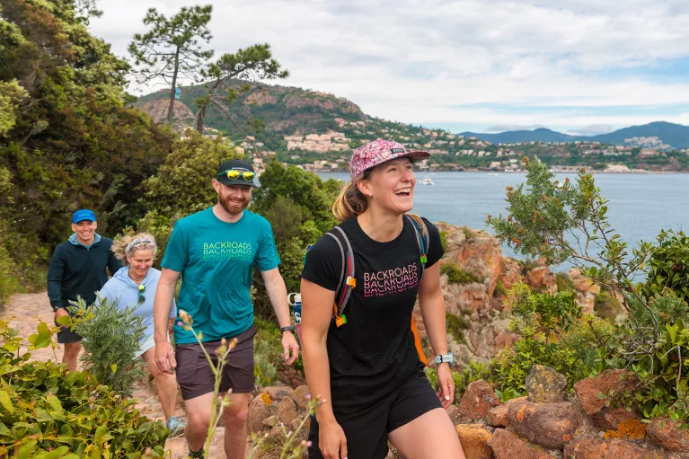 Group of people smiling while hiking on a trail with the ocean in the background