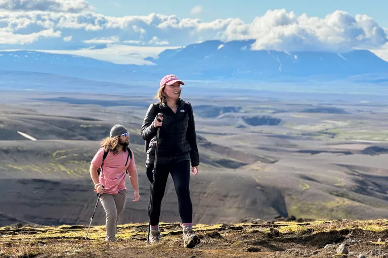 Man and woman ascending a dirt trail with large hills in the background