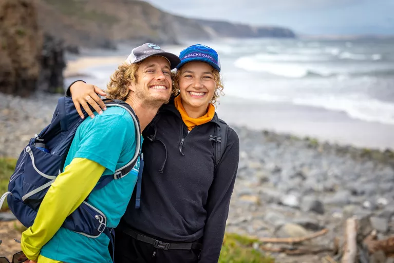 Man and woman smiling and hugging in front of a beach