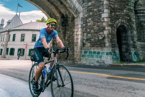 Man riding a bike on a road under a stone arc in a city