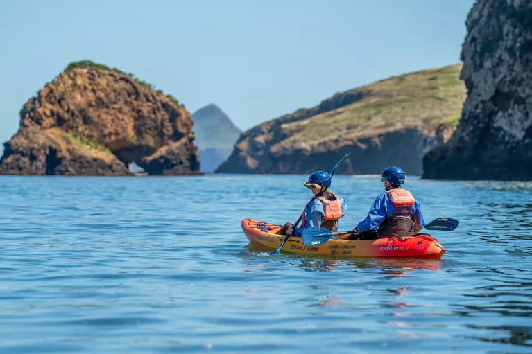 Two people paddling on an orange kayak in the middle of a lake