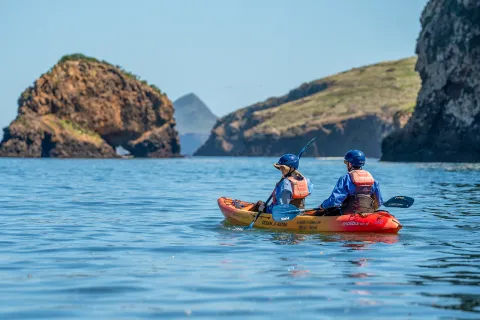 Two people paddling on an orange kayak in the middle of a lake