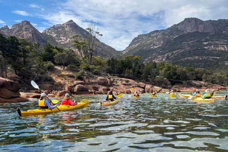 Group of people paddling in individual, yellow kayaks in a lake